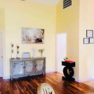 A cozy living room with wooden flooring, adorned by a cabinet and decorative items on a yellow wall backdrop.
