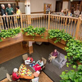 A community space with people gathered in a seating area surrounded by plants, viewed from an upper level.