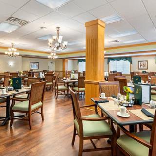 A spacious dining area with neatly arranged tables and chairs, featuring elegant chandeliers and warm wood flooring.