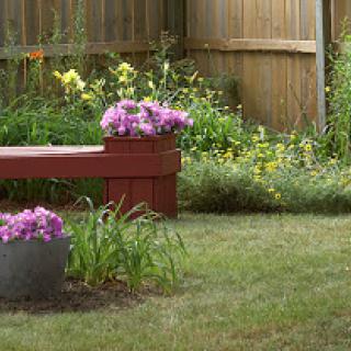 A serene garden scene featuring a wooden bench adorned with colorful flowers, surrounded by lush greenery.