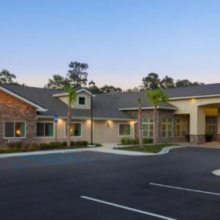 A modern building with a parking lot in the foreground, surrounded by trees.