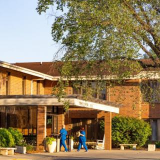 A hospital building with medical staff walking outside in the sunlight.