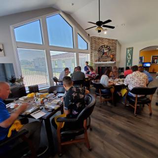 A group of people enjoying a meal together in a well-lit room with large windows.