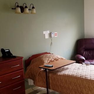 A cozy hospital patient room with a bed, nightstand, and seating area.