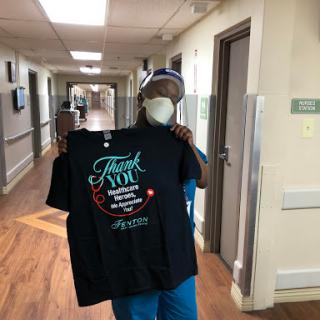 A healthcare worker proudly displays a 'Thank You' shirt in the hospital hallway.