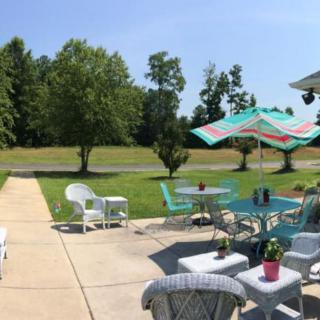 A sunny patio with wicker furniture and a garden umbrella overlooking a grassy lawn and trees.