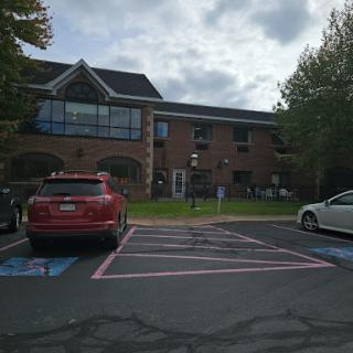 A view of a building with parked cars in front under a cloudy sky.