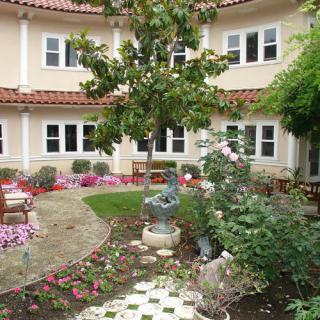 A charming courtyard garden with colorful flowers, a small fountain, and surrounding architecture.