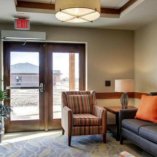 A cozy living room with a comfortable armchair and sofa, lit by a warm ceiling lamp near a glass door.