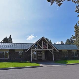 A single-story building with a large entrance and a metal roof, surrounded by trees under a clear blue sky.