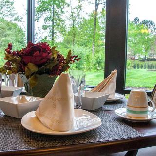 A beautifully set dining table with folded napkins, flower centerpiece, and a scenic window view.