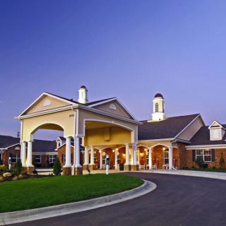 A well-lit building entrance with a driveway during the evening.