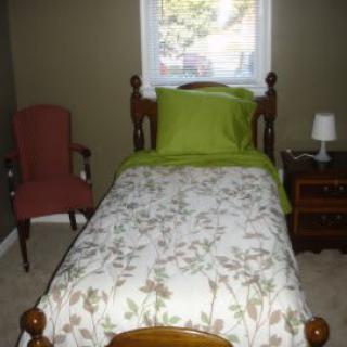 A cozy bedroom with a single bed, floral bedding, and a bedside table.