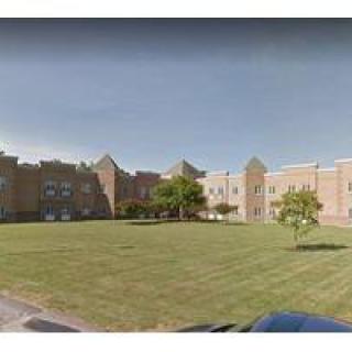 A brick school building with a large lawn and trees under a clear sky.