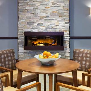 A cozy modern living room with a stone fireplace and a wooden table surrounded by chairs.