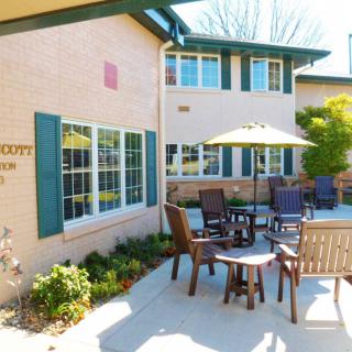 A cozy outdoor patio area with tables, chairs, and umbrellas in a garden setting.