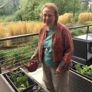 A woman tending to her balcony garden with lush greenery in the background.