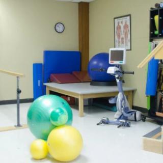 A physical therapy room equipped with various exercise tools such as therapy balls and an exercise bike.