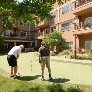 Two men enjoying a game of golf on an outdoor putting green at a retirement community.