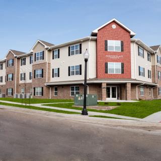 A modern apartment building on a street corner with well-maintained landscaping.