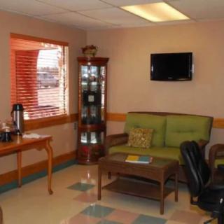 A cozy waiting room with a sofa, coffee table, TV, and a window with curtains.