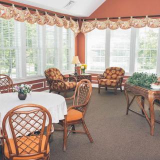A cozy sunroom with large windows, decorated with wicker furniture and a white tablecloth.