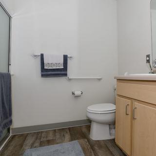 A modern bathroom featuring a toilet, sink with cabinetry, and a shower with towels.