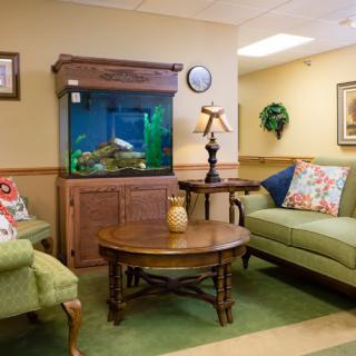 A cozy living room with an aquarium, green sofas, and a wooden table.