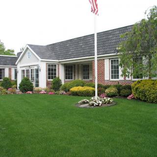 A charming single-story home with a well-maintained lawn and colorful garden, featuring an American flag.