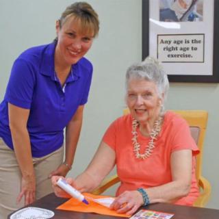An elderly woman engaged in an activity with the assistance of a caregiver.