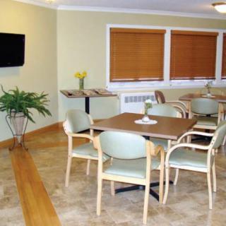 A cozy dining area with tables and chairs, featuring a wall-mounted television and windows with blinds.