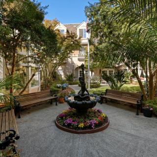 A tranquil courtyard featuring a central fountain surrounded by lush greenery and benches.