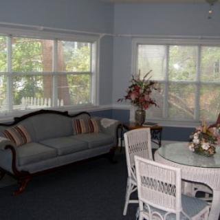 A cozy living room with a classic sofa, dining set, and large windows allowing natural light.
