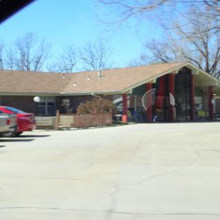 A view of a residential building with parked cars and playground equipment nearby.