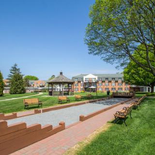 A scenic park area with benches, a gazebo, and a pathway surrounded by greenery and buildings in the background.
