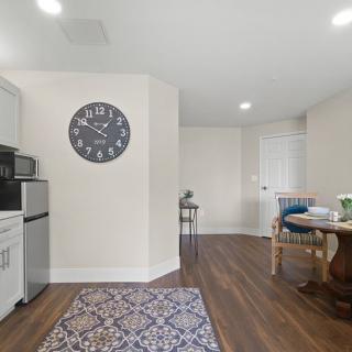 A modern kitchen interior with a wall clock, wooden flooring, and a dining table.