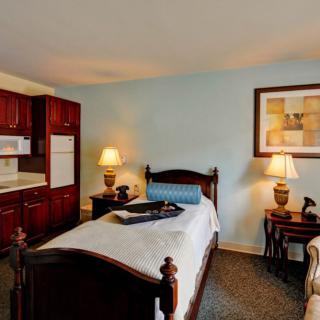 A cozy bedroom with a single wooden bed, elegant lamps, and a kitchenette.