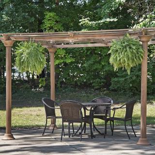 An outdoor patio with a wooden pergola, featuring a table and chairs surrounded by greenery.