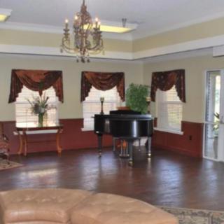 A cozy living room featuring a grand piano, elegant chandelier, and large windows with curtains.