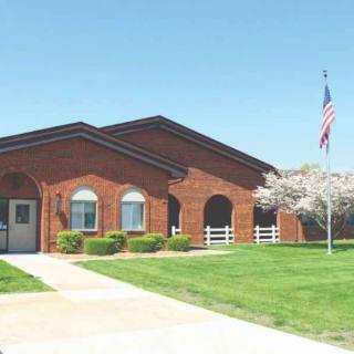A brick building with an American flag, surrounded by a well-maintained lawn and blossoming tree.