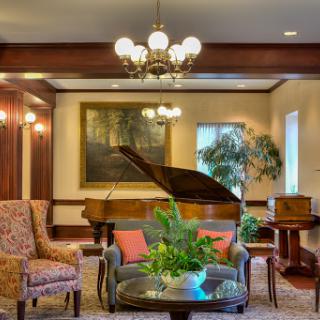 A cozy and elegant lounge area featuring a grand piano, stylish furniture, and decorative plants.