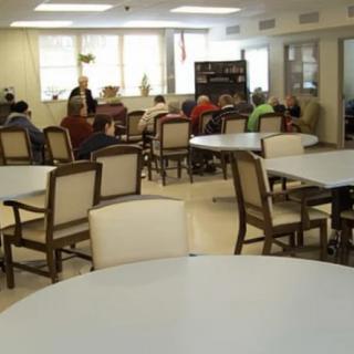 A dining area with empty tables and chairs, and a group of people sitting in the background.