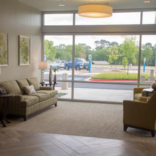 A cozy lobby area featuring a sofa and chairs with ample natural light from large windows.