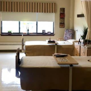 A hospital room with two neatly made patient beds and a large window.