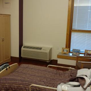 A view of a hospital room featuring a bed, an air conditioning unit, and personal photographs displayed on a ledge.