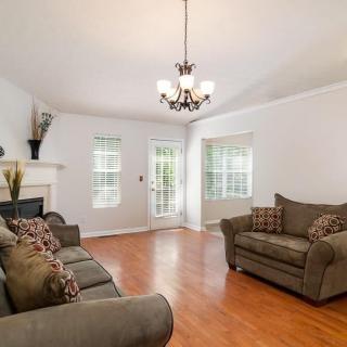 A bright and cozy living room with sofas, wooden flooring, and a chandelier.