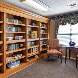 A cozy reading room with a well-stocked bookshelf, an armchair, and a table near a window.