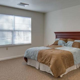 A cozy bedroom with a neatly made bed and natural light coming through the window blinds.