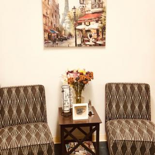 A cozy living space with patterned chairs, a small wooden table with flowers, and a Parisian-themed painting.