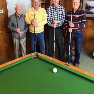 A group of four seniors standing around a pool table, each holding a cue stick.